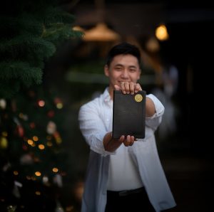 Man holding Bible with Biblica Bible Buddy sticker on the front, next to Christmas tree